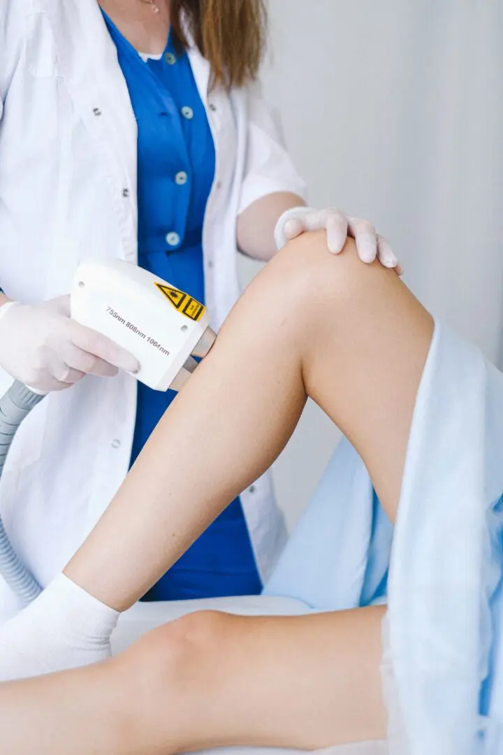 A doctor is using an electric device to treat the leg of a woman.
